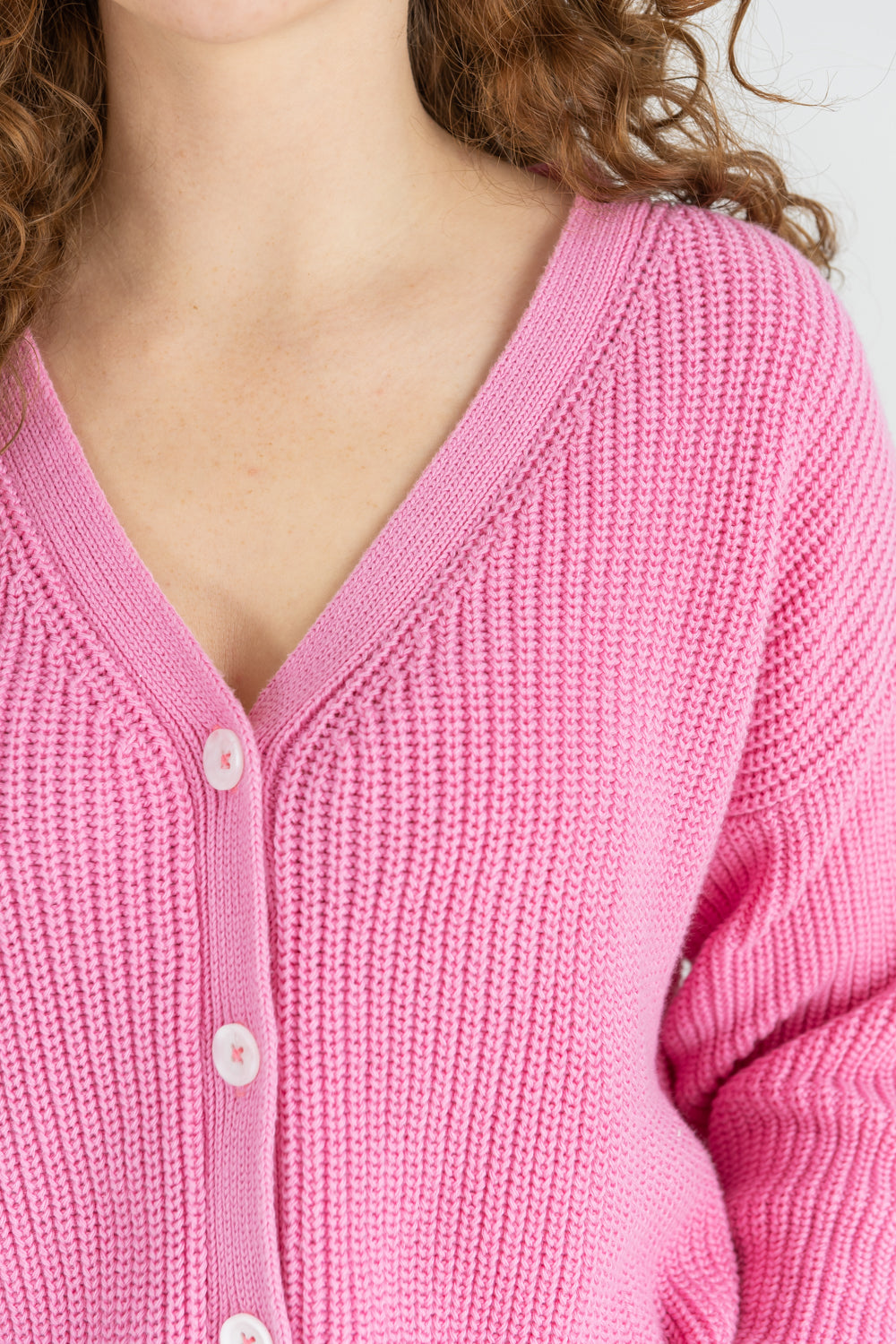 Pinke verkürzte Strickjacke mit hellen Knöpfen.